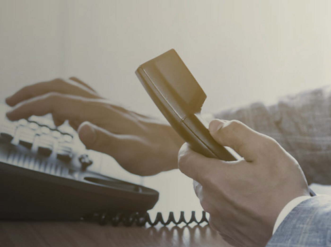 A hand picking up the telephone handset at the office desk